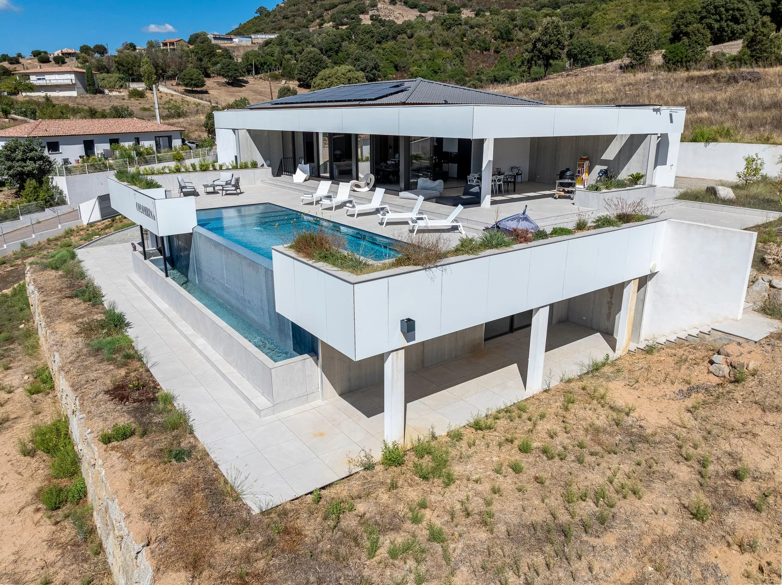 Villa vue de trois quarts en drone, piscine miroir et terrasse en surplomb de la pente
