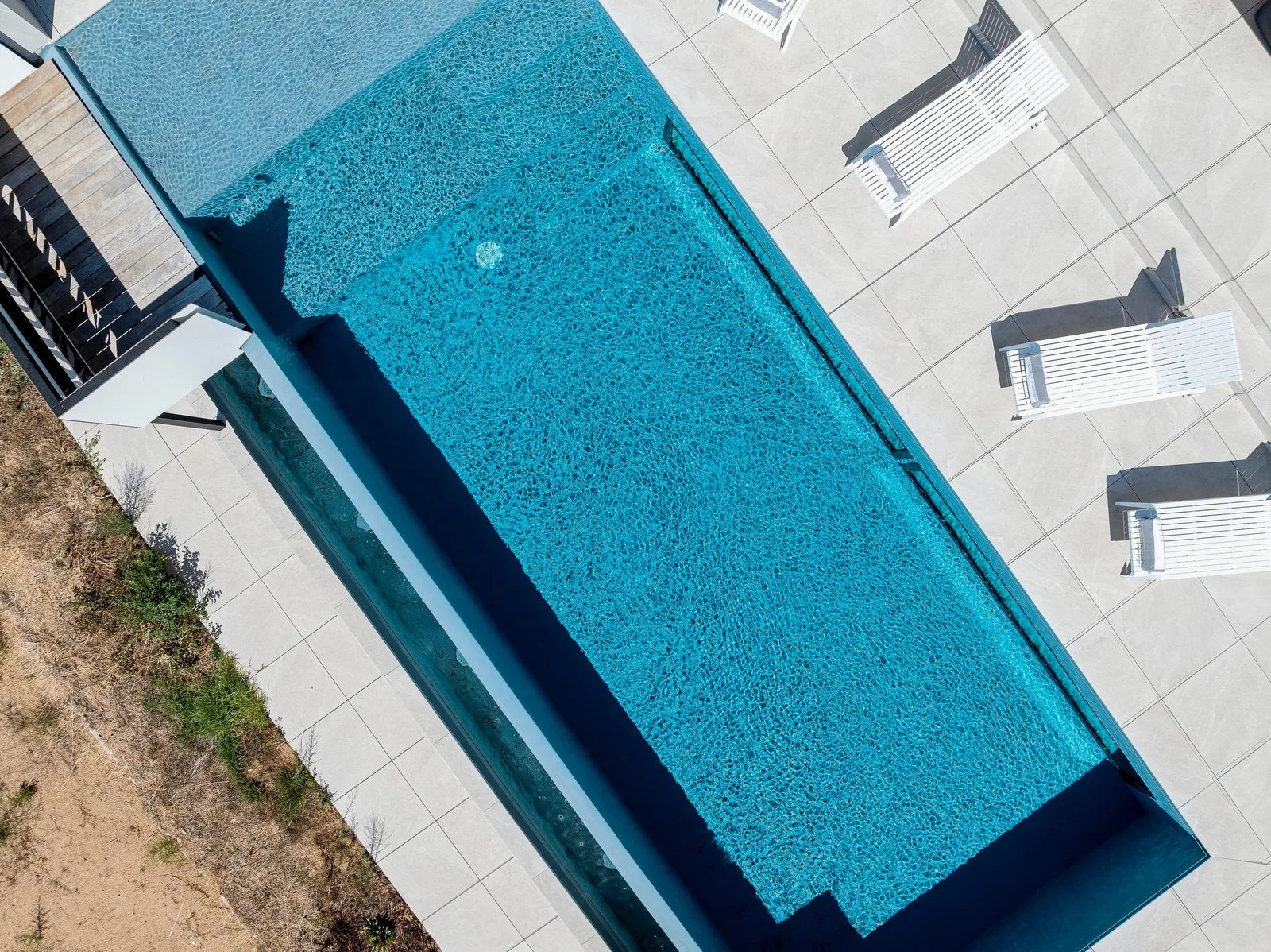 Vue zénithale de la piscine à débordement turquoise et des transats sur la terrasse