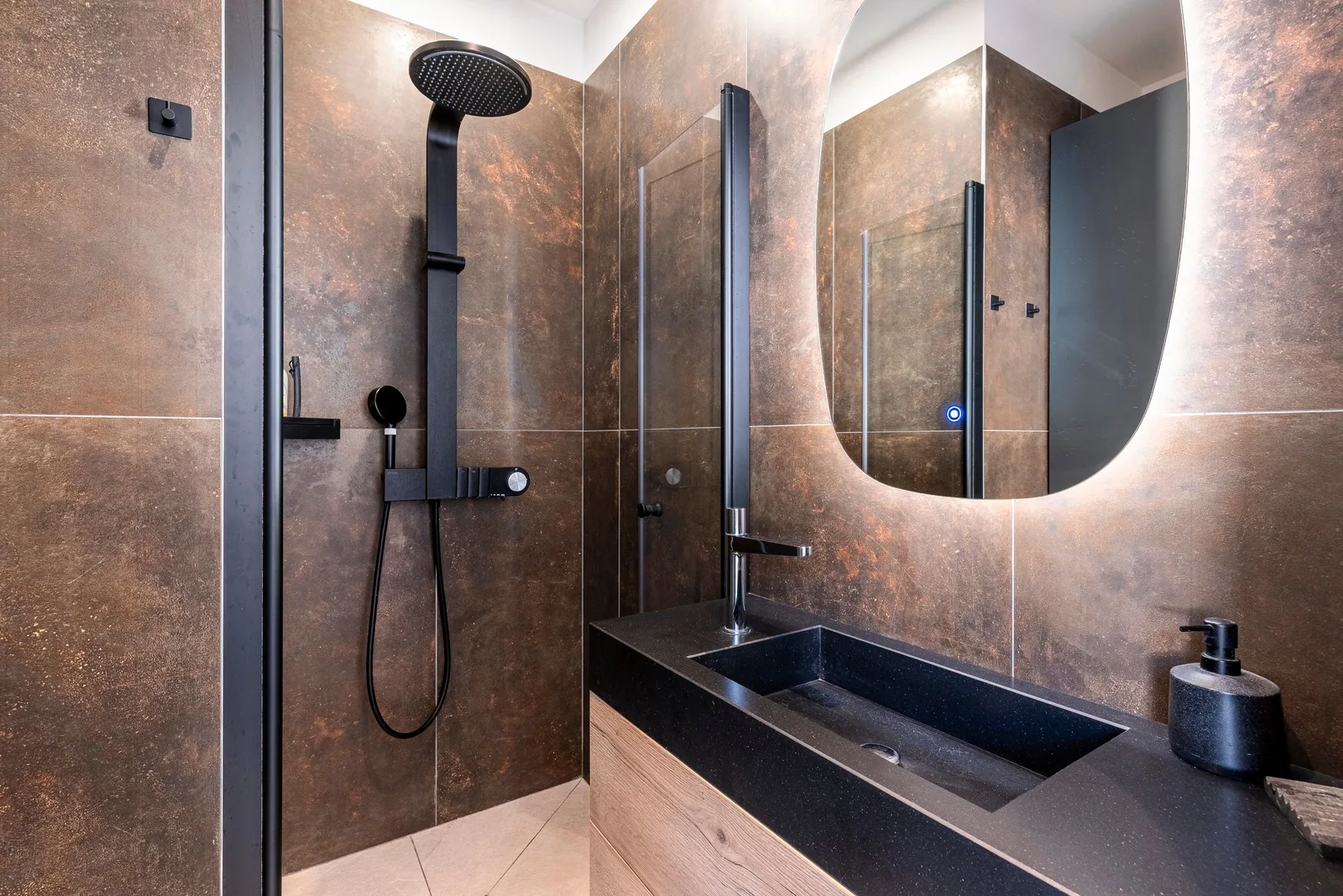 Salle d'eau aux carreaux effet rouille, vasque noire, meuble bois et douche à l'italienne