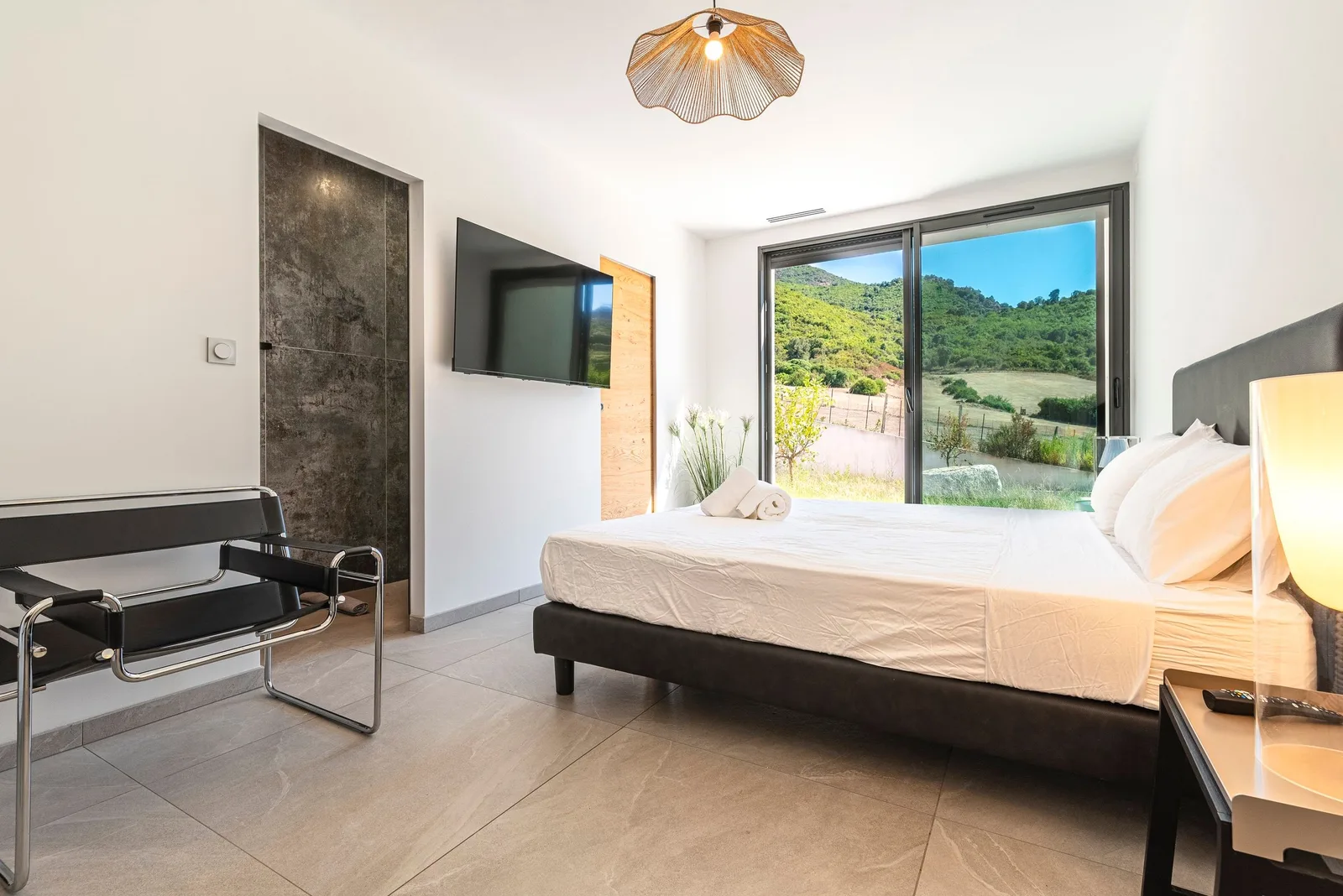 Chambre avec lit double, fauteuil Wassily et baie vitrée ouverte sur le maquis