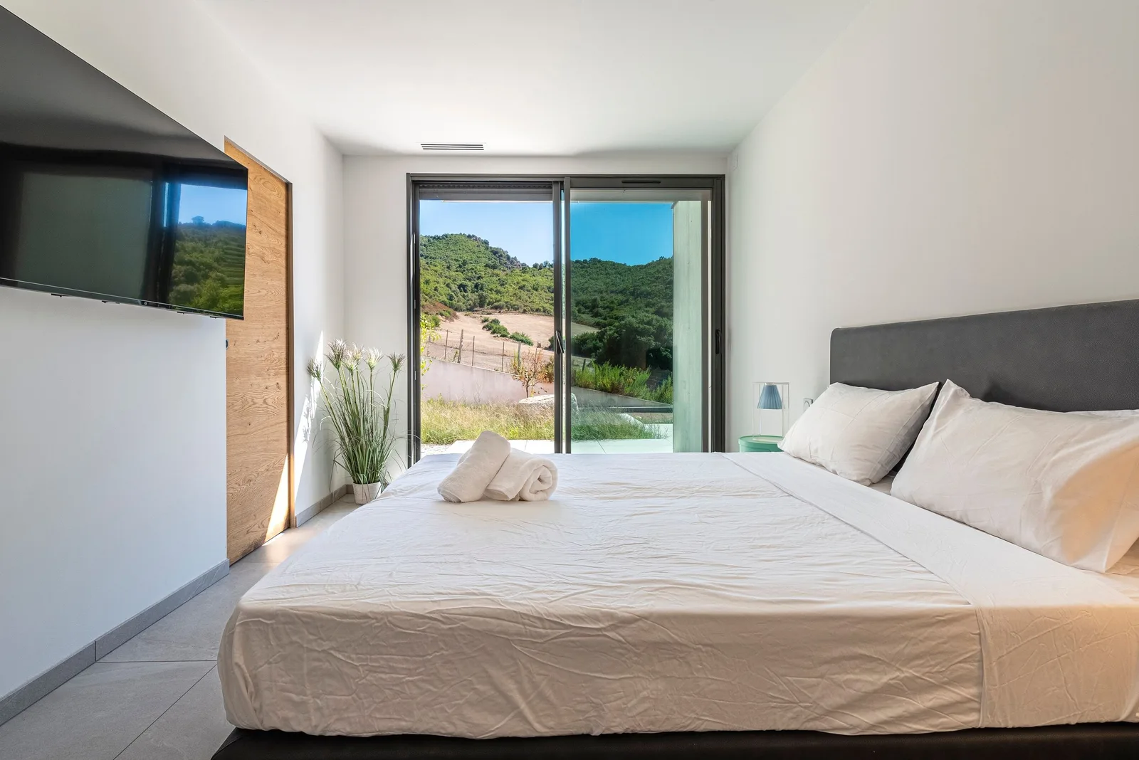 Chambre lumineuse, lit double et baie vitrée donnant accès à la terrasse et aux collines