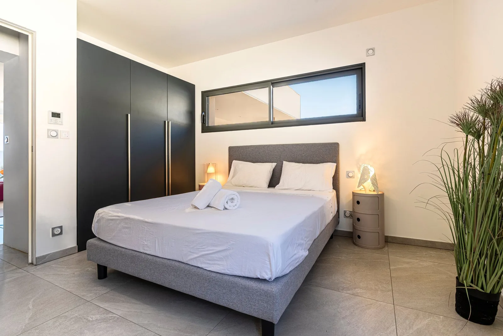 Chambre avec lit king-size, placards noirs, bandeau vitré et plante en pot