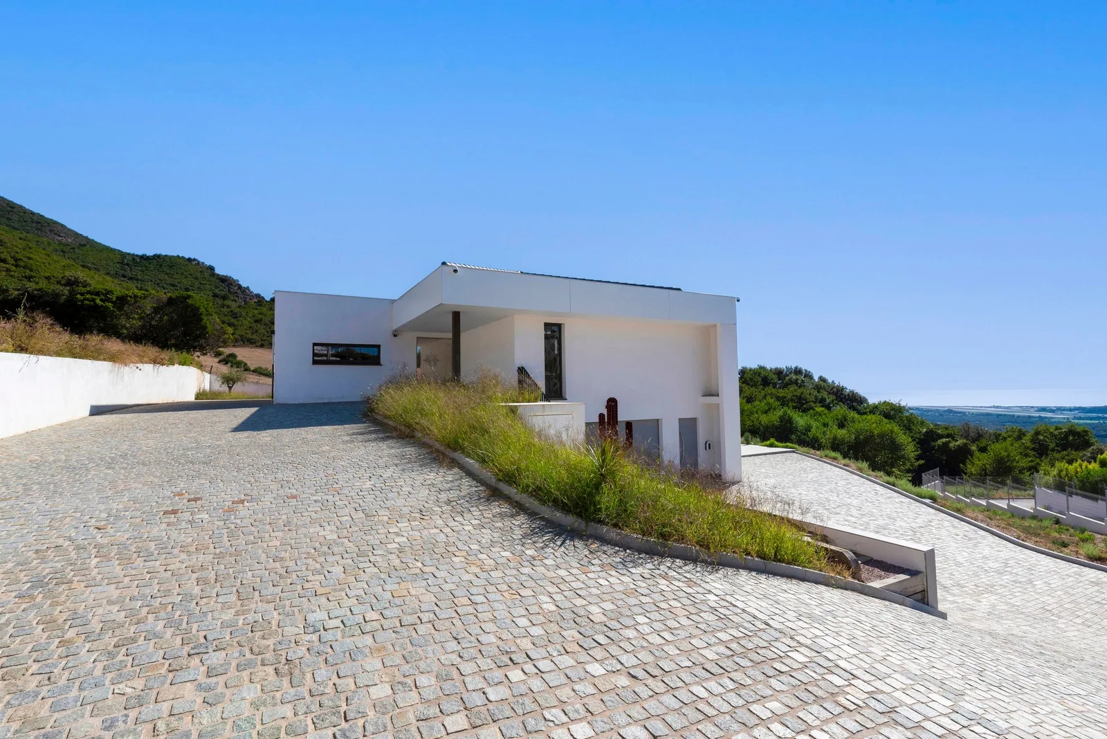 Allée pavée menant à l'entrée de la villa, façade blanche et vue vers la mer