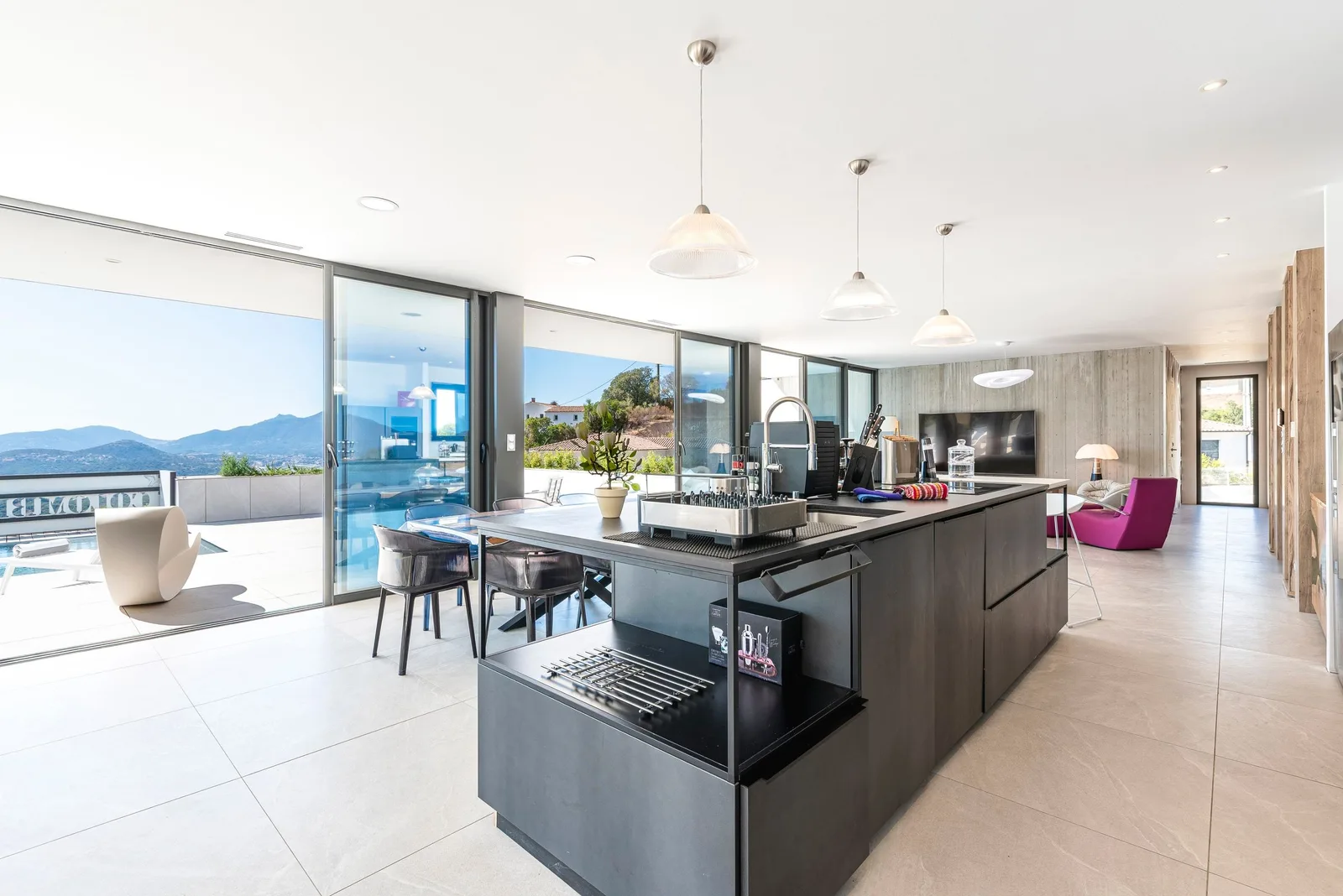 Cuisine anthracite ouverte sur le salon, baies vitrées et vue sur la mer et les collines