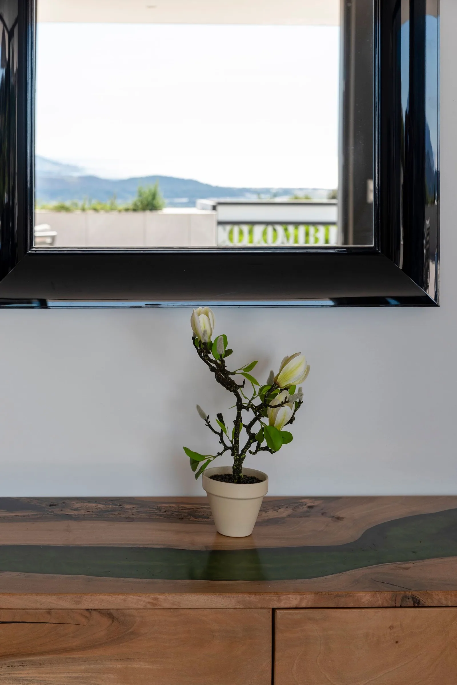Branche de magnolia en pot sur une console en bois à rivière de résine, fenêtre sur le maquis