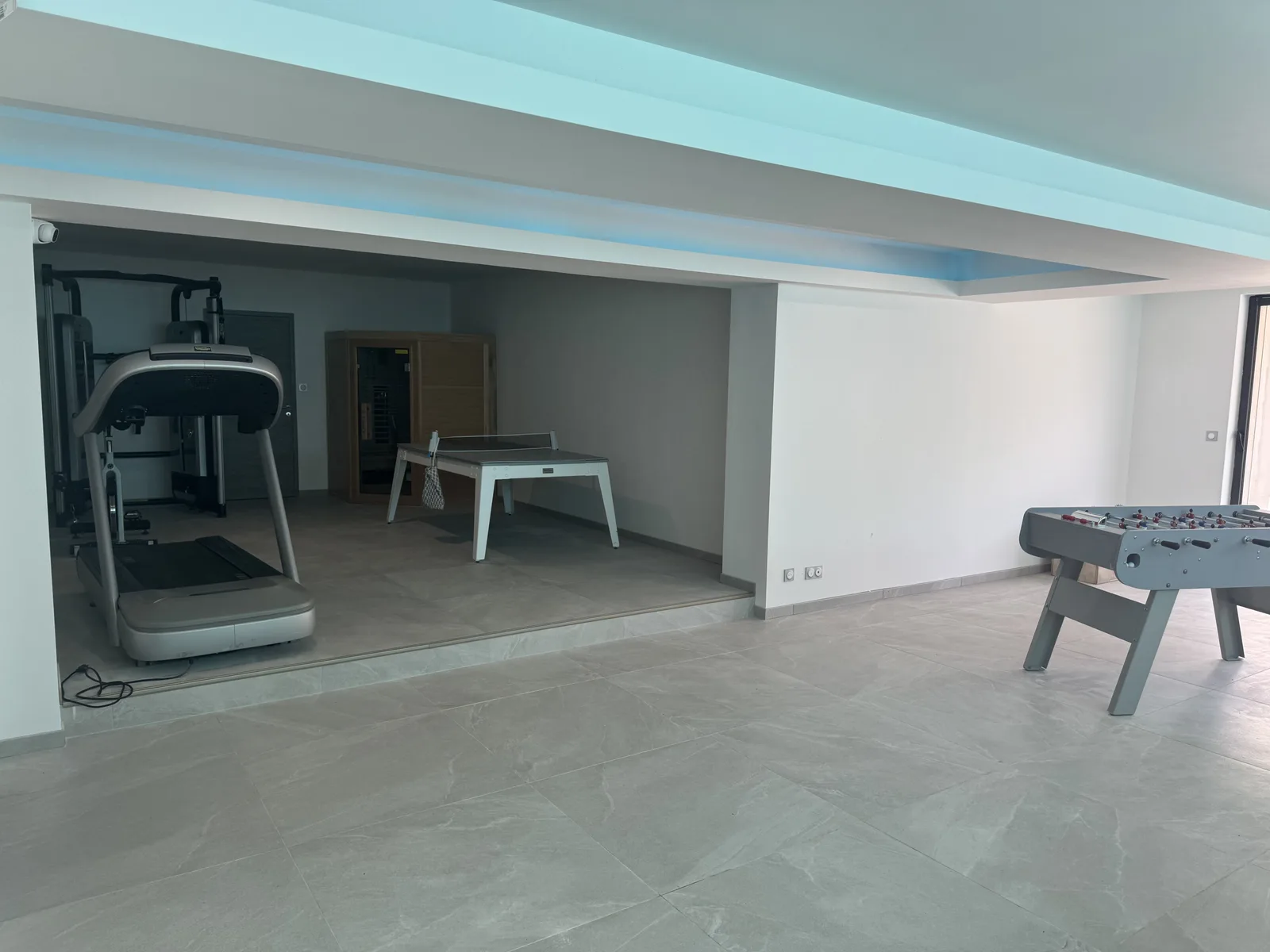 Espace détente en sous-sol ouvert sur la salle de jeux, sauna et table de ping-pong au fond
