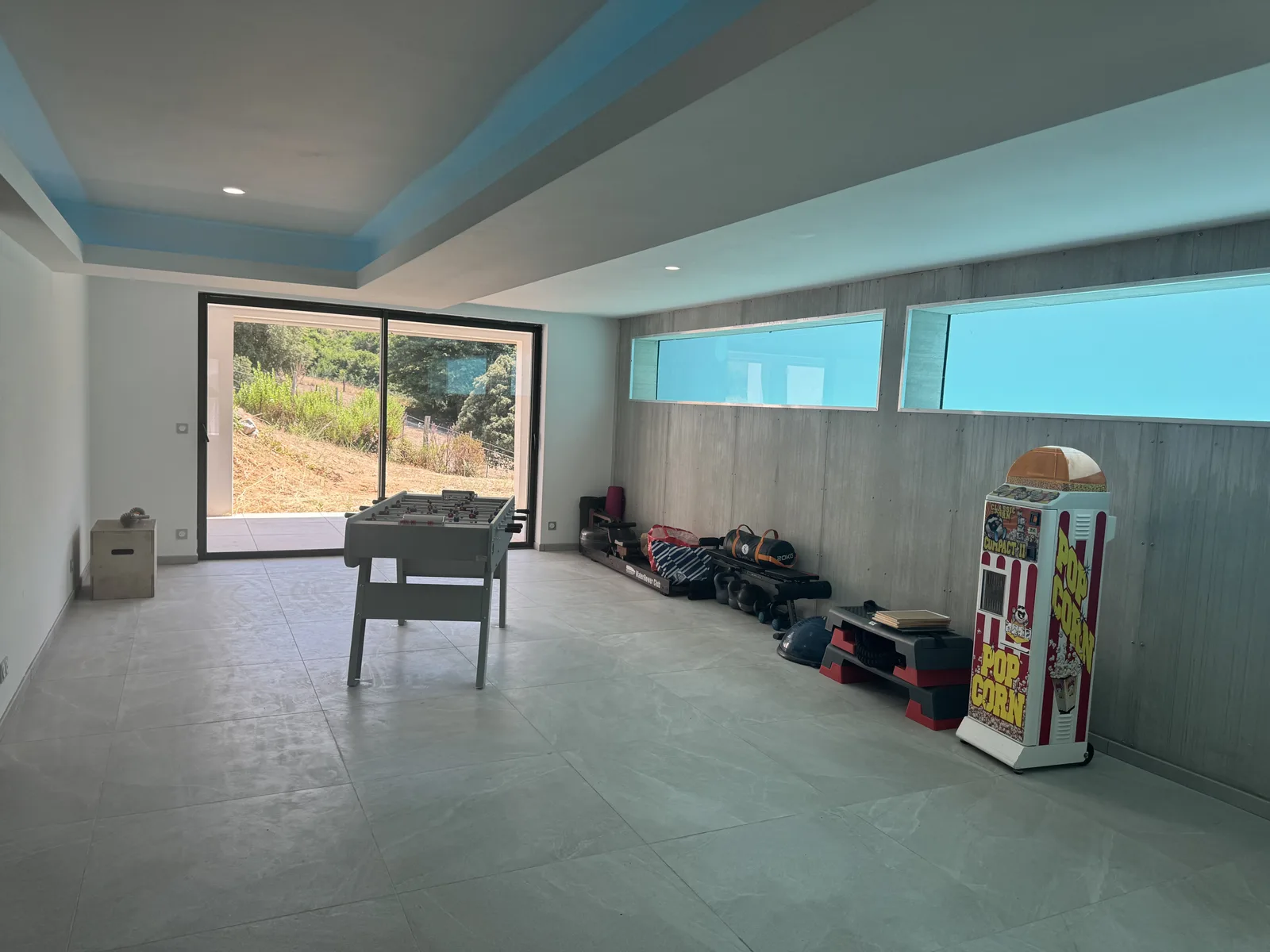 Salle de jeux ouverte sur le maquis par une baie vitrée coulissante, baby-foot et matériel de fitness