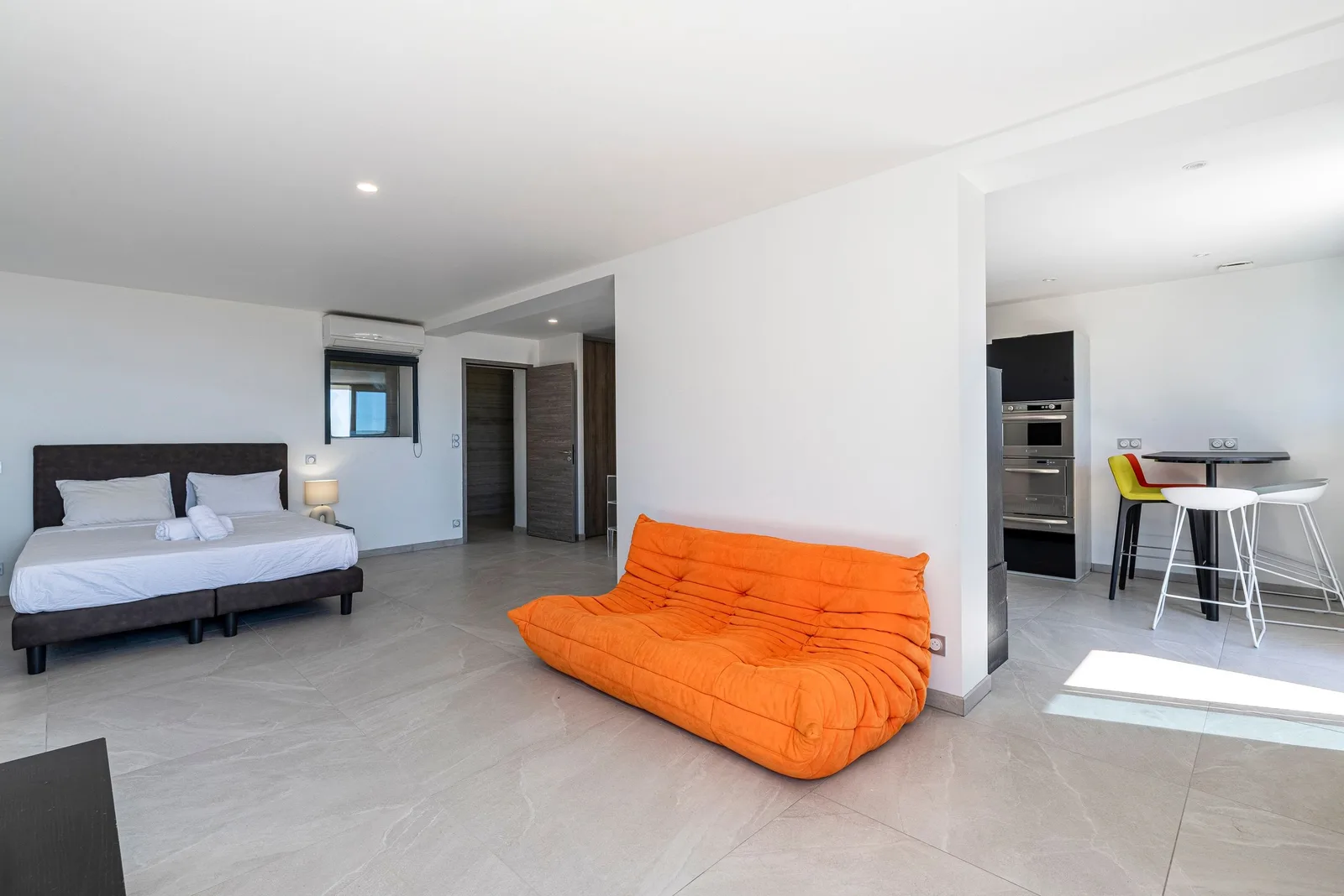 Studio indépendant : lit double, canapé Togo orange et coin repas avec tabourets hauts