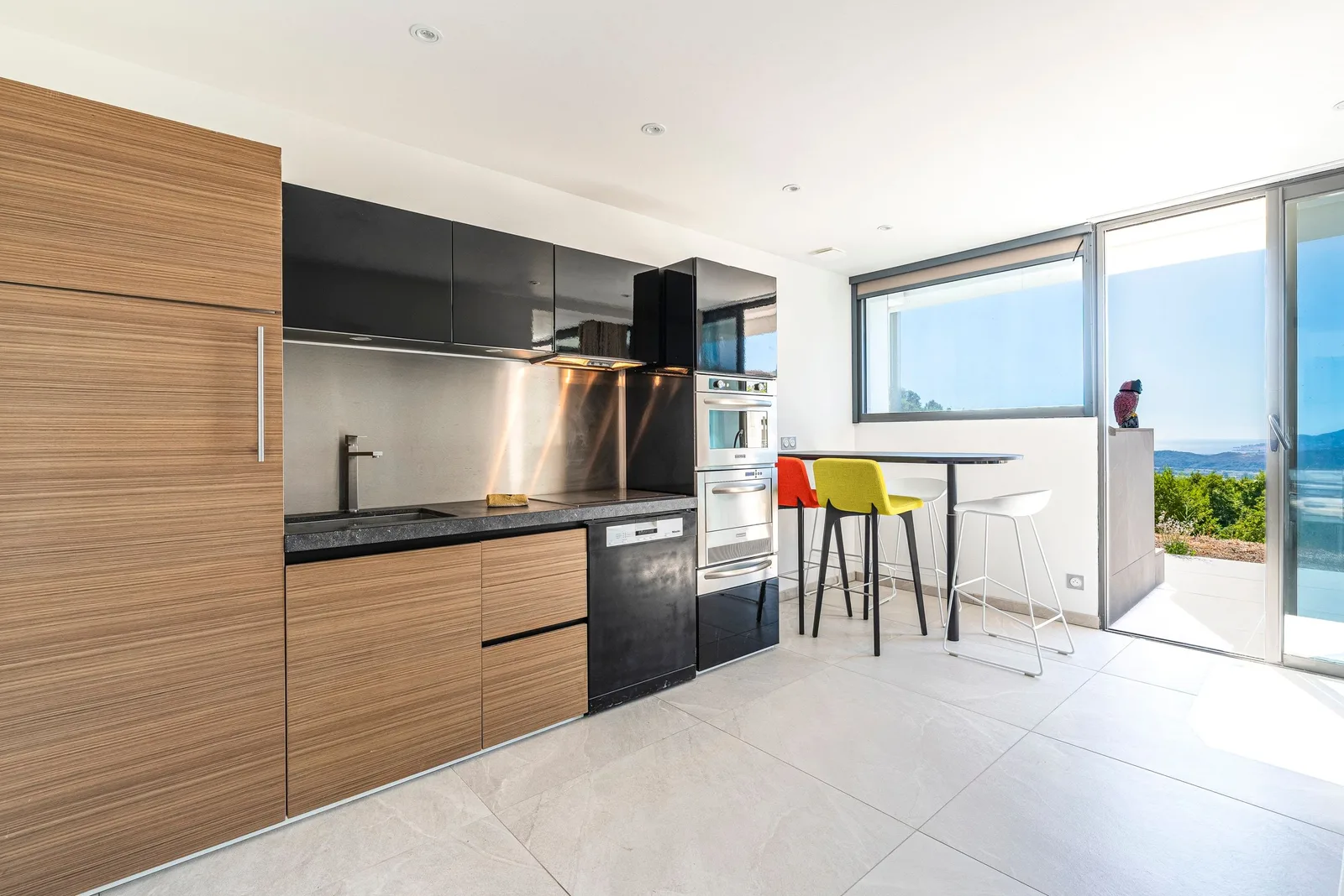 Kitchenette du studio en bois clair, four et lave-vaisselle, baie vitrée avec vue dégagée