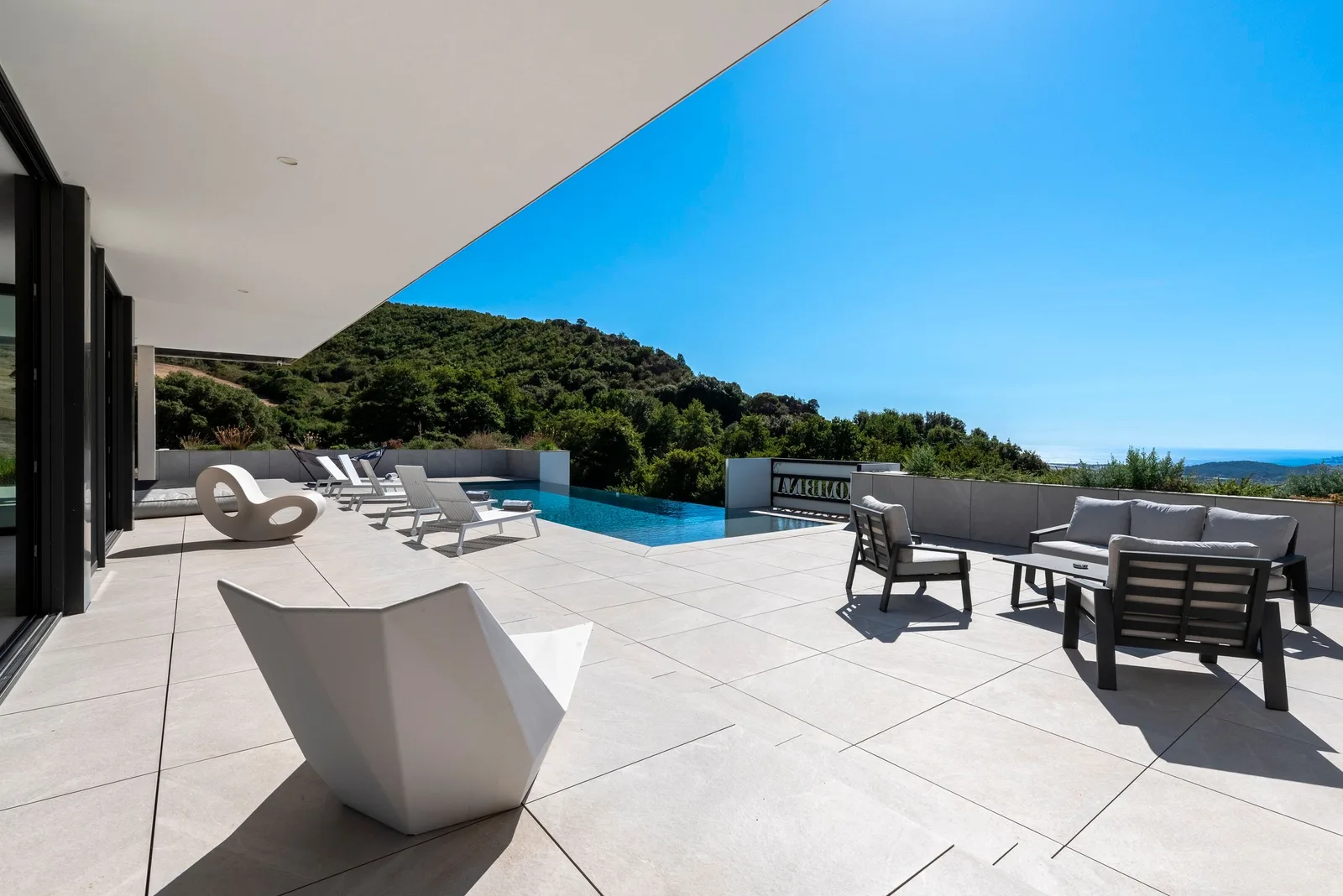 Fauteuil facetté blanc et salon de jardin sur la terrasse, piscine à débordement face au maquis