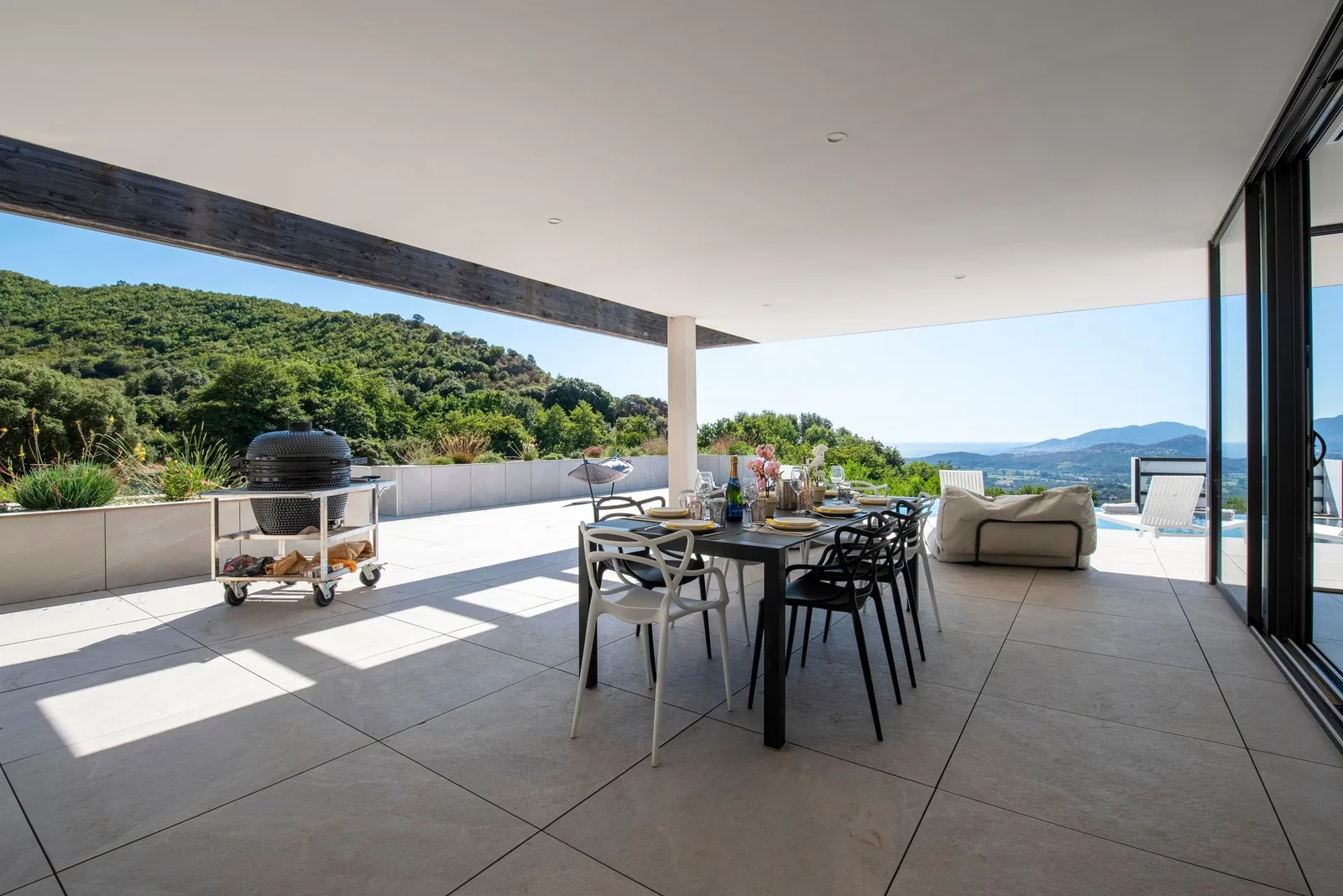 Terrasse couverte avec plancha sur chariot et table à manger face aux collines