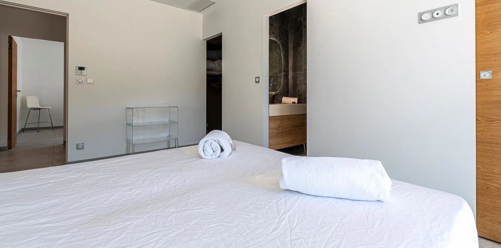 Chambre épurée aux murs blancs, lit king-size et salle d'eau attenante habillée de béton