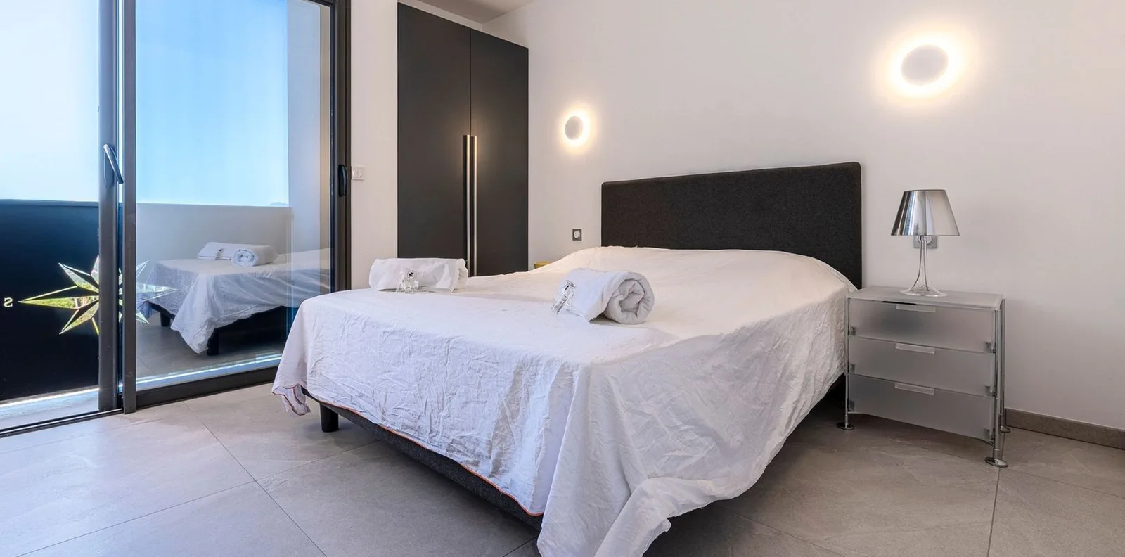 Chambre lumineuse avec lit double, dressing noir et appliques design donnant sur la terrasse