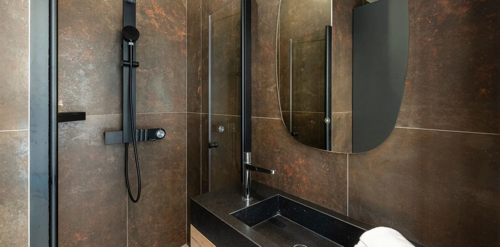 Salle d'eau aux carreaux effet métal rouillé, douche à l'italienne et vasque en pierre noire