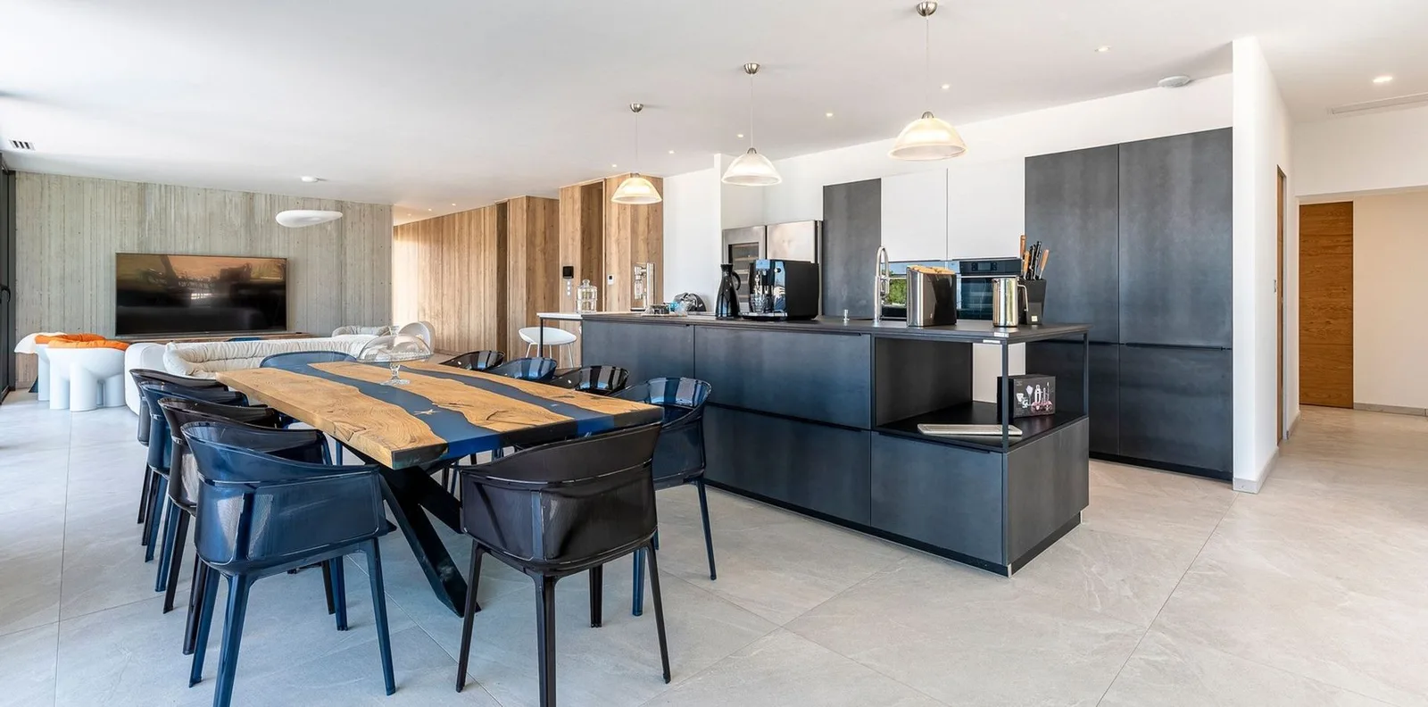 Cuisine anthracite ouverte sur la salle à manger, table en bois à rivière de résine et chaises noires