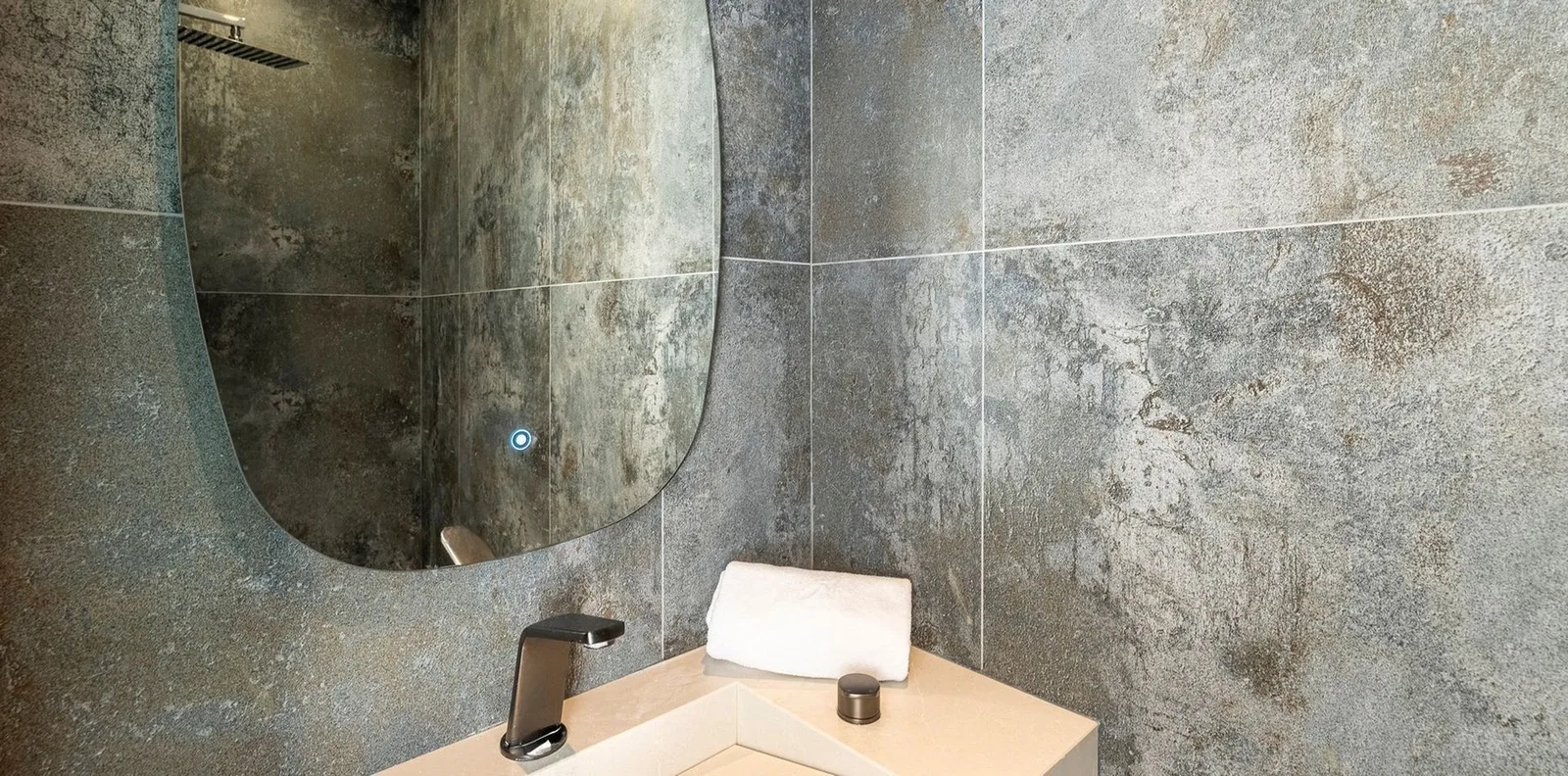Salle d'eau aux carreaux gris effet béton patiné, miroir organique rétroéclairé et mitigeur noir