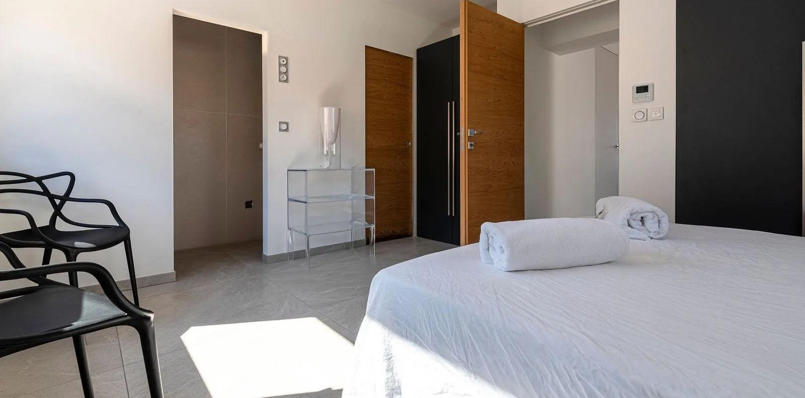 Chambre baignée de soleil, portes en bois clair, dressing noir et console transparente design