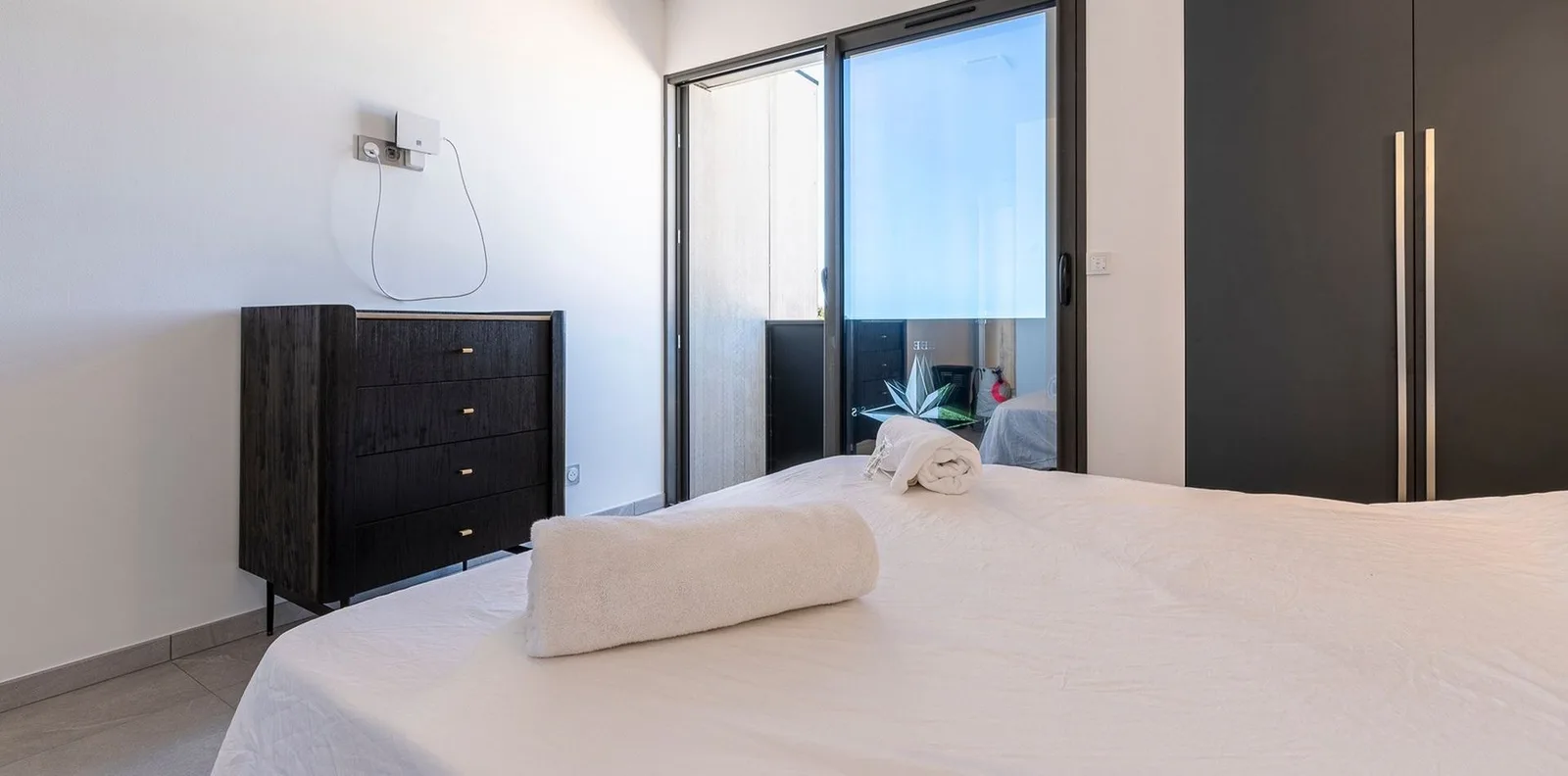 Chambre contemporaine avec commode en bois noir, dressing miroir et lit habillé de linge blanc