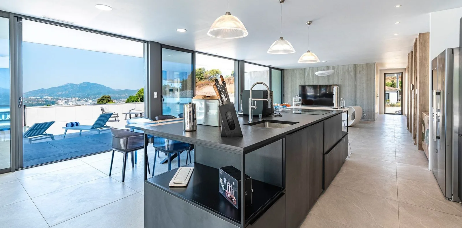 Cuisine anthracite à grand îlot ouverte par des baies sur la terrasse et les collines du golfe d'Ajaccio