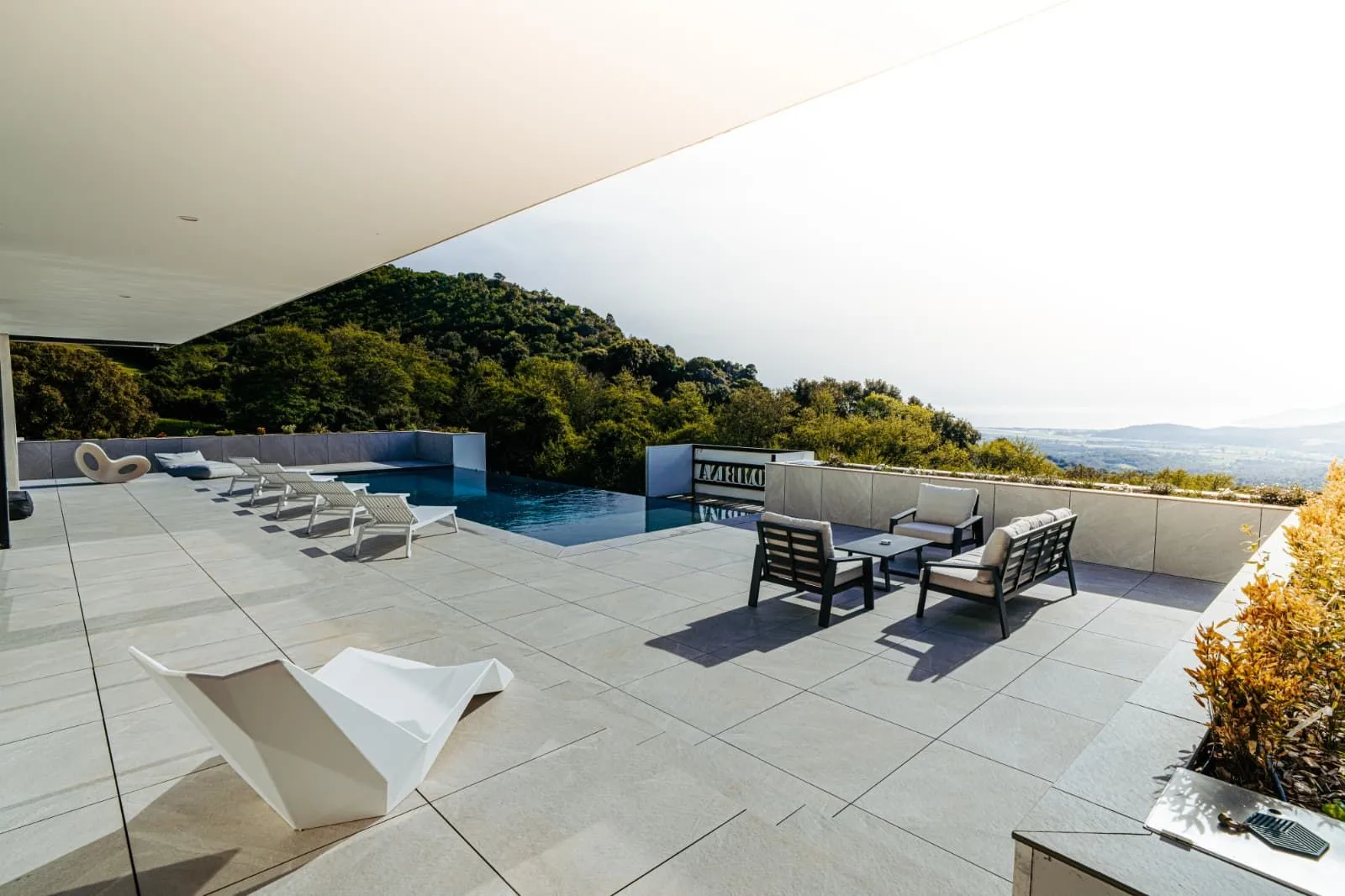 Terrasse ensoleillée aux transats et salon d'extérieur près de la piscine à débordement