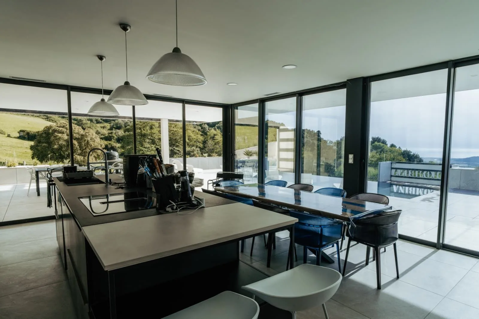 Cuisine design avec îlot central, longue table et suspensions face aux collines verdoyantes